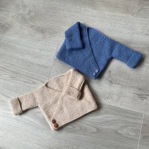 Puede incluir: Dos cárdigans de punto para bebé, uno de color beige claro y otro de color azul claro. Ambos cárdigans tienen un estilo de envoltura y un cierre de botón.