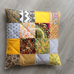 Può includere: Un cuscino patchwork giallo, grigio e marrone con una varietà di motivi floreali e geometrici.