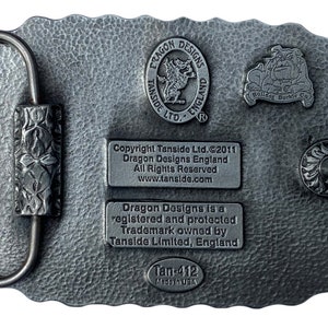 May include: A rectangular, silver-colored belt buckle with a textured surface. The buckle features a loop and a decorative clasp. The back of the buckle has several embossed logos and text, including "Dragon Designs England" and "Bulldog Buckle Co."