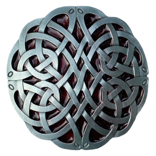 Könnte beinhalten: Eine silberne Gürtelschnalle mit einem keltischen Knoten und einer roten Emaille-Einlage. Die Schnalle ist rund und hat ein detailliertes Design.