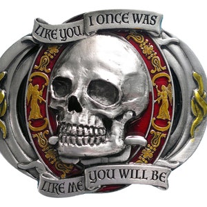 K&ouml;nnte beinhalten: Silberfarbene Metallschnalle mit einem Totenkopf und dem Text "LIKE YOU I ONCE WAS LIKE ME YOU WILL BE". Die Schnalle hat rote und goldene Akzente, mit Engelsfiguren an den Seiten.