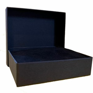 May include: An open, black gift box with a textured exterior and a soft, dark interior. The box is rectangular with a hinged lid, perfect for jewelry or small gifts. The box is set against a white background.