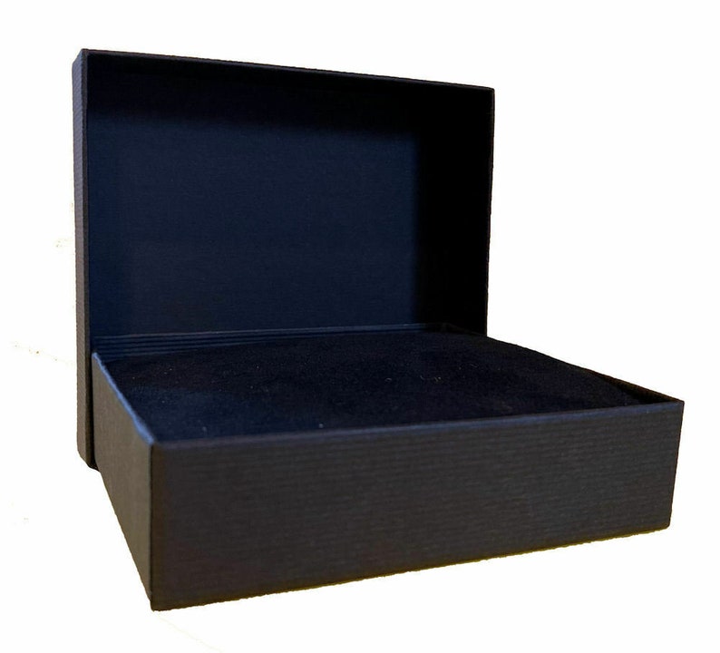 May include: An open, black gift box with a textured exterior and a soft, dark interior. The box is rectangular with a hinged lid, perfect for jewelry or small gifts. The box is set against a white background.