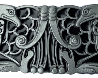 Puede incluir: Una hebilla de cinturón de plata con fondo de esmalte negro. La hebilla presenta un diseño de nudo celta con dos cabezas de pájaro estilizadas a cada lado.