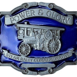 May include: A silver belt buckle with a blue enamel background. The buckle features a steam engine with the words "Power & Glory Steam Rally Commemorative" around the engine.