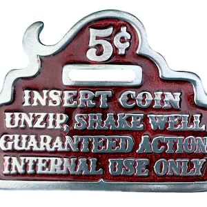Puede incluir: Una cartera de monedas de metal roja con borde plateado. La cartera tiene una ranura para insertar una moneda y el texto "5¢ INSERT COIN UNZIP SHAKE WELL GUARANTEED ACTION INTERNAL USE ONLY".