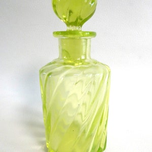 May include: A clear, yellow-green glass bottle with a twisted design and a matching twisted knob stopper.