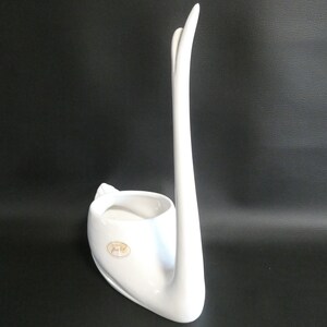 May include: White ceramic swan planter with a rounded base and a long, curved neck. The planter has a small oval label on the side.