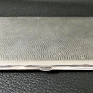 Peut inclure: Un étui à cigarettes en argent avec une surface texturée.