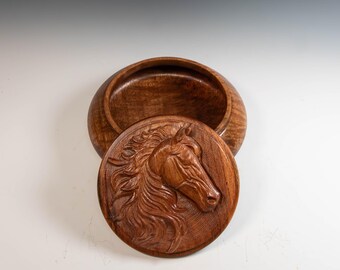 May include: A handcrafted wooden box with a lid featuring a detailed relief carving of a horse's head. The box is open, revealing the interior. The wood has a rich, warm brown color.