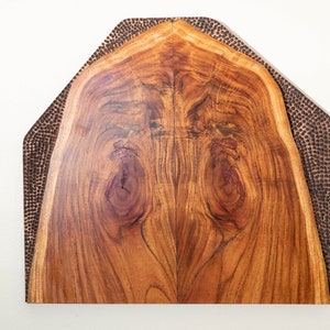 May include: A wooden wall art piece with a natural wood grain finish. The wood is surrounded by a border of hammered copper.