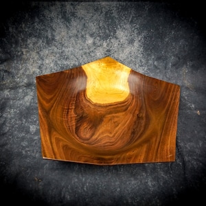 May include: A wooden bowl with a distinctive shape, crafted from wood with a natural grain. The bowl's design incorporates a contrast of colours, with a lighter, golden interior and a darker, rich brown exterior. The bowl's dimensions are approximately 30 cm in length.