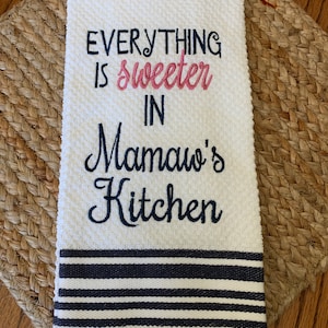 May include: White kitchen towel with black stripes and embroidered text that reads "Everything is sweeter in Mamaw's Kitchen".
