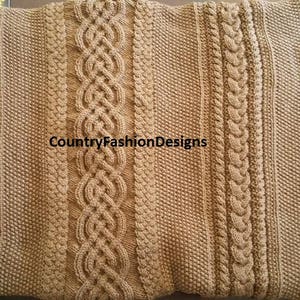 May include: A brown knitted throw blanket with a variety of cable knit patterns. The blanket has a woven label that reads "CountryFashionDesigns".