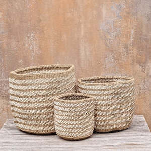Peut inclure: Trois paniers tressés de tailles différentes. Les paniers sont faits de fibres de couleur naturelle avec des rayures blanches horizontales. Ils sont disposés sur une surface en bois vieilli, sur un fond brun clair texturé.
