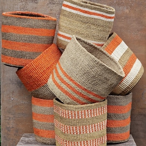 Peut inclure: Une collection de paniers tissés cylindriques présentant divers motifs à rayures dans des tons orange, beige et blanc. Les paniers sont empilés ensemble, affichant différents designs de tissage horizontal et vertical avec une finition texturée.