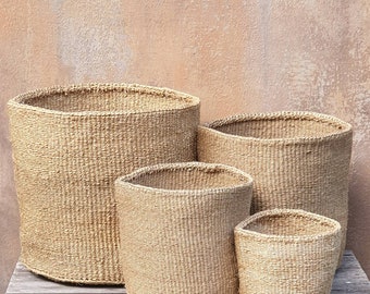 Puede incluir: Cuatro cestas tejidas naturales de diferentes tamaños, hechas de un material marrón claro, están dispuestas en una fila sobre una superficie de madera. Las cestas son todas de forma cilíndrica y tienen un fondo ligeramente redondeado.