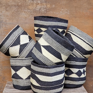 May include: A set of six black and white woven baskets with geometric patterns. The baskets are made from natural materials and have a rustic, handcrafted look.