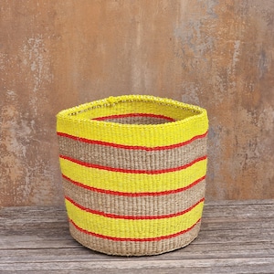 May include: A cylindrical woven basket featuring horizontal stripes in bright neon yellow, natural tan, and vibrant red. The basket has a wide, open top and a sturdy, structured base, showcasing a detailed, textured weave pattern throughout its exterior.