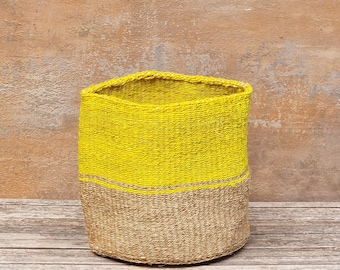 May include: A woven basket with a cylindrical shape. The top half is bright yellow, and the bottom half is a natural tan color. A thin, horizontal tan stripe separates the two colors. The basket is made of a textured material.