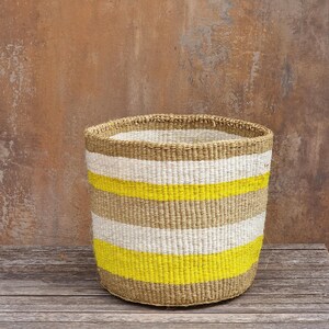 May include: A cylindrical woven basket featuring horizontal stripes in natural tan, bright white, and vibrant neon yellow. The basket has a sturdy, open-top design with a consistent, textured weave pattern throughout the entire exterior surface.