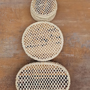 May include: Three woven round and oval coasters in a checkered pattern of brown and white. The coasters are made of natural materials and have a rustic look.