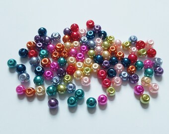 May include: A large assortment of colorful round beads in various shades of blue, green, red, orange, pink, purple, and cream. The beads are scattered on a white surface.