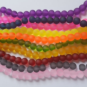 May include: A collection of colourful frosted glass beads in various shades of purple, blue, pink, yellow, orange, green, red, grey, and pink. The beads are arranged in rows, creating a rainbow effect.