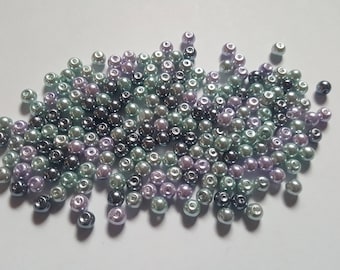 May include: A pile of small, round beads in shades of green, purple, and dark gray. The beads have a pearlescent sheen, reflecting light. These beads are suitable for jewelry making and craft projects.