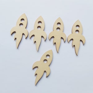 May include: Five unfinished wooden rocket ship cutouts with a sixth cutout in the center. The cutouts are all the same size and shape, and they are all made of light brown wood.