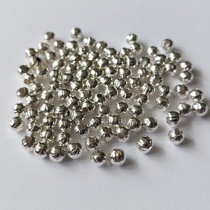 May include: A pile of silver-coloured metal beads with a textured, rounded design. The beads are small and have a hole in the centre for stringing.