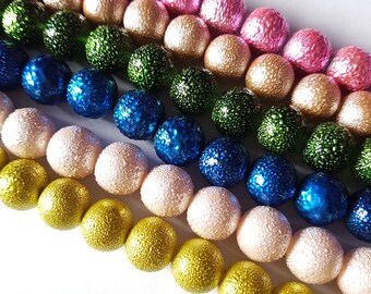May include: A strand of colorful beads with a textured surface. The beads are arranged in rows of pink, gold, green, blue, and gold.