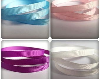 May include: Four spools of ribbon in different colors: light blue, pink, purple, and white. The ribbon is a textured, grosgrain style.