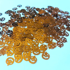 Op de afbeelding: Een grote stapel gouden glitter-pompoen confetti. De confetti heeft de vorm van een pompoen met een jack-o'-lantern gezicht.