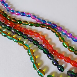 May include: Assortment of oval-shaped glass beads in various iridescent colours, including blue, pink, green, orange, and yellow. The beads are arranged in rows, creating a colourful and eye-catching display.