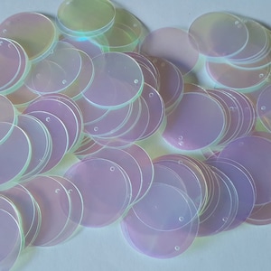 Op de afbeelding: Een stapel iriserende ronde pailletten in een lichtpaarse en witte kleur. De pailletten hebben een gat in het midden om te naaien.