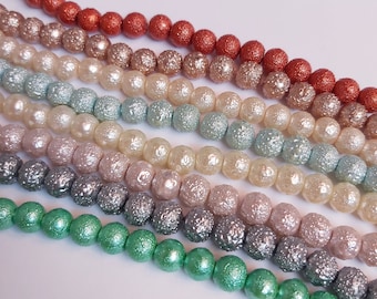 May include: A collection of colorful, textured beads in shades of green, gray, pink, and orange. The beads are arranged in rows, creating a visually appealing pattern.
