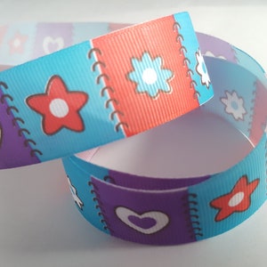 May include: A blue, purple, and red ribbon with a patchwork design featuring hearts, flowers, and stars. The ribbon has a white background and is decorated with a stitched seam.