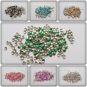 May include: Assortment of square-shaped metal embellishments in various colours, including black, turquoise, gold, green, pink, purple, and silver. The embellishments are small and have a raised, pyramid-like shape.