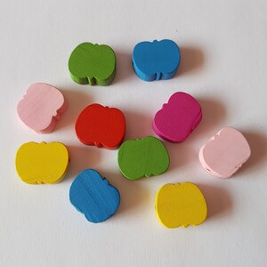 Pode incluir: Dez contas de madeira em forma de maçã em várias cores, incluindo rosa, amarelo, verde, azul e vermelho.