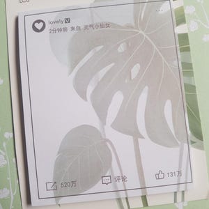 May include: A square sticky note featuring a social media interface design with a heart icon, the text "lovely", and Chinese characters. The background of the note displays a faint, light green illustration of a monstera leaf pattern.