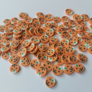 May include: A large group of orange and white pumpkin-shaped Halloween sprinkles with green jack-o'-lantern faces.