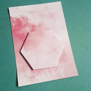 May include: A hexagonal sticky note pad with a pink watercolor wash design, mounted on a rectangular backing card. The card features the text "WATERCOLOR & GEOMETRY" at the top and "GARDEN PALACE" with a small logo at the bottom in white lettering.