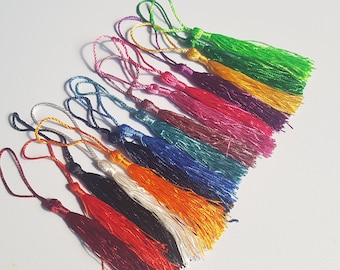 May include: A collection of 12 colourful tassels in a variety of colours including green, yellow, purple, pink, blue, teal, black, white, orange, red, and maroon.