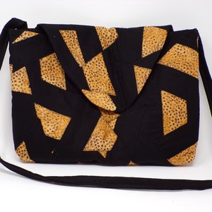 Può includere: Una borsa a tracolla in patchwork nero e marrone con un motivo geometrico. La borsa ha una tracolla lunga e una chiusura a lembo.