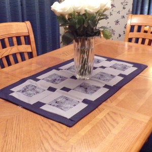 May include: A wooden dining table with a blue and white patterned table runner. A vase with white roses is in the centre of the table.
