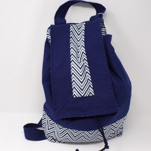 Peut inclure: Un sac à dos bleu marine avec un motif en chevron blanc et bleu sur le fond et un rabat avec un motif en chevron sur le devant.