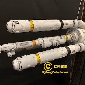 May include: A detailed model spacecraft, predominantly white and grey with gold and orange accents. The model has multiple cylindrical sections and intricate detailing, suggesting a science fiction theme. The image includes the text "COPYRIGHT BigBangCollectables".