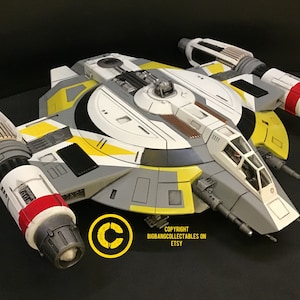 Puede incluir: Un modelo detallado de una nave espacial U-Wing de Star Wars, pintada en un esquema de colores amarillo, blanco y gris. El modelo tiene una cabina, dos motores y una variedad de armas.