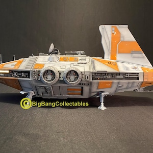 Może przedstawiać: Szczegółowy model statku kosmicznego, z kolorystyką biało-szaro-pomarańczową. Model posiada skomplikowane detale mechaniczne, w tym silniki, skrzydła i kokpit. Statek kosmiczny jest prezentowany na ciemnej powierzchni.